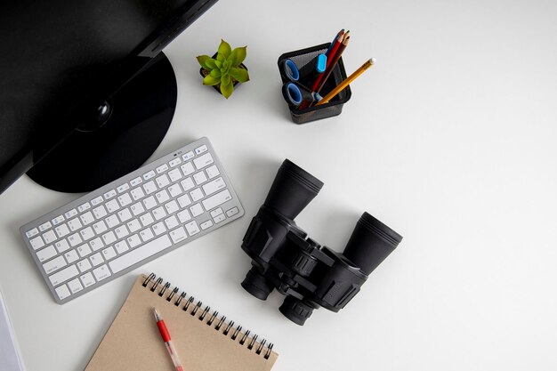 Binoculars lying on the desktop near the computer on a white background Top view flat lay