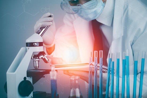 Biochemical research scientist working with a microscope for the virusDoctor man write a history of the experimental results in a  laboratory glassware containing chemical liquid for design