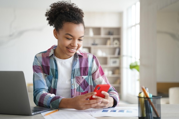 Biracial teen girl hold phone distracted from studying Social network addiction overuse of gadgets