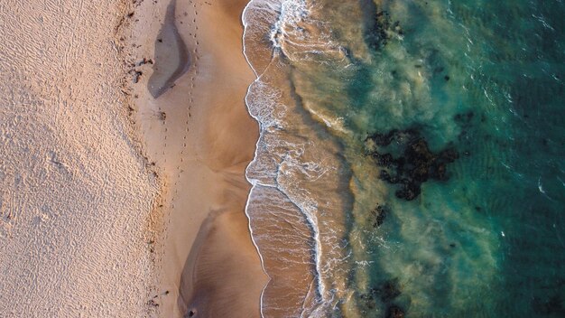 Bird's eye view of crystal clear ocean waves crashing against a sandy coastline