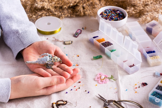 Bird woven from beads in children's hands among boxes with beads