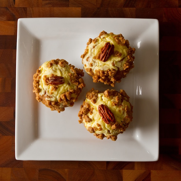 Birds eye view of three orange muffins topped with frosting and a pecan on a white plate on a tabl