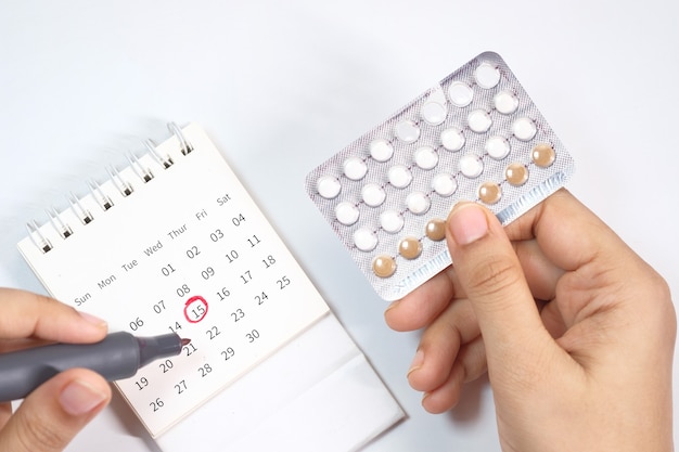 Birth control pills , calendar and notepad on table .