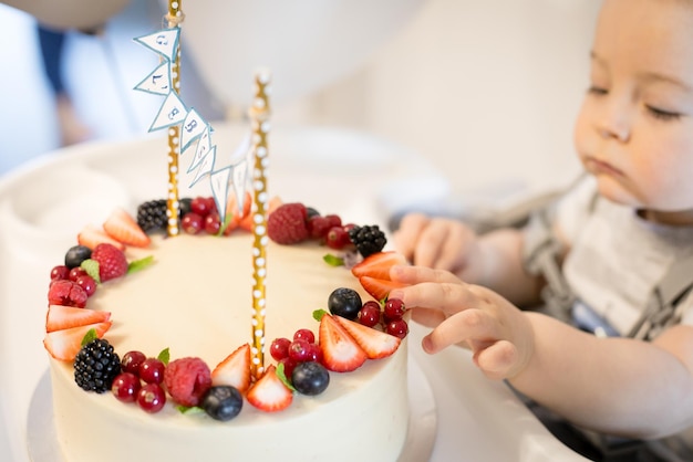 Birthday berry cake and caucasian baby boy celebrating first birthday at home