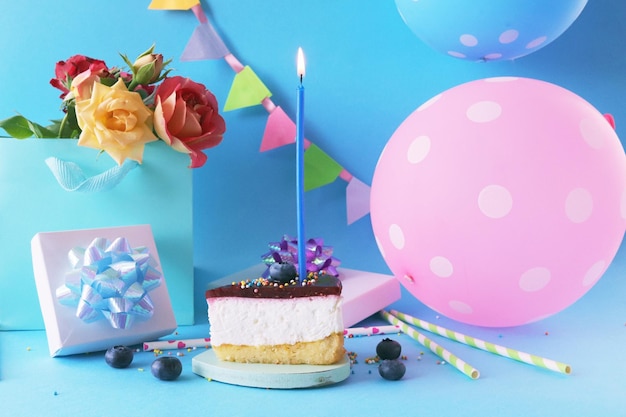 Birthday cake with candles flowers balloons and gift box on blue background