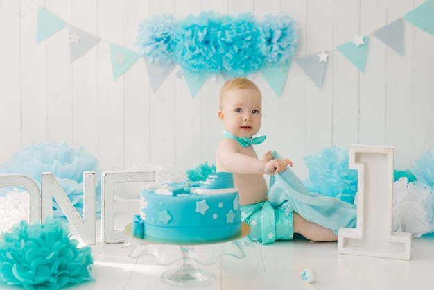 Birthday child 1 year old boy, baby sitting with blue garlands and number one in a suit and bowtie