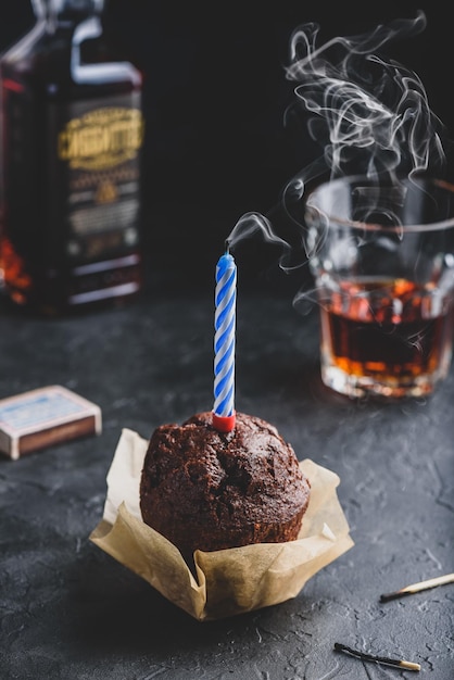 Birthday chocolate muffin with smoking candle on dark concrete background