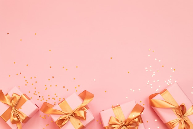 Birthday or Christmas gift boxes with gold bow on a pink background. Flat lay, top view, copy space.