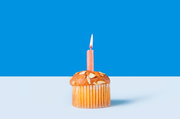 Photo birthday cupcake with glowing candles on white table with blue background closeup