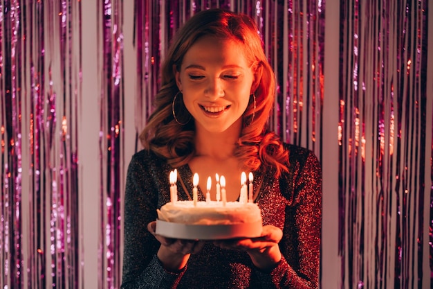 Birthday event Happy festive woman Holiday wish Happy inspired lady feeling amazed holding cake with candle lights on shimmering purple cascade curtain background