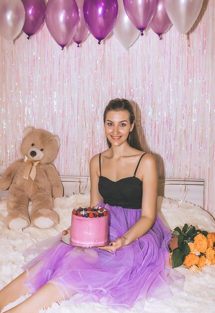 Birthday girl closeup in purple skirt. Young pretty woman is sitting on the bed with purple air balls in her hand