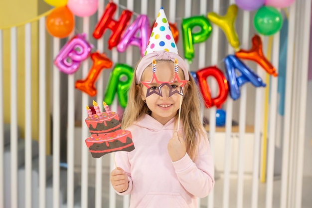 The birthday girl in a festive hat, with a pipe and props is having fun