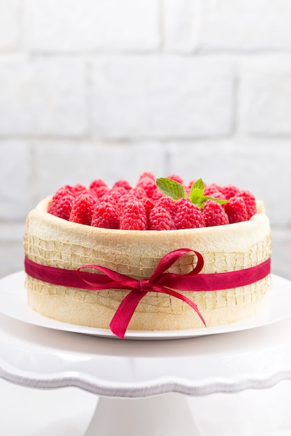 Birthday spongecake with raspberries decorated ribbon and bow on a white cake stand