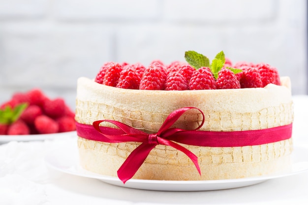 Birthday spongecake with raspberries decorated white ribbon and bow on a light background