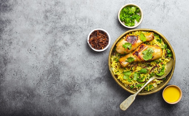 Biryani chicken, traditional dish of Indian cuisine, with basmati rice, fried onion, fresh cilantro in bowl on gray rustic stone background. Authentic Indian meal, top view, close-up, space for text