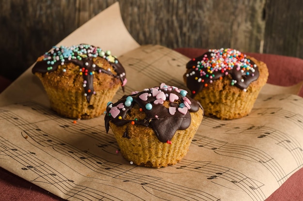 Biscuit cupcakes on paper sprinkled with chocolate with colored sprinkles on a wooden background