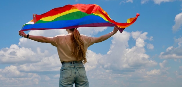 Bisexual lesbian woman transgender holds LGBT flag against blue sky with clouds on a sunny day and Celebrate Bisexuality Day or National Coming Out Day