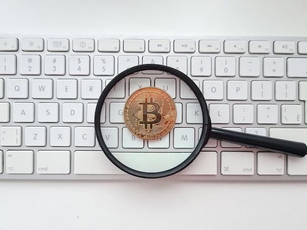 Bitcoin pending magnifying glass and bitcoin coin on white computer keyboard