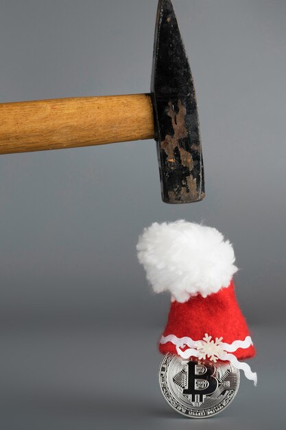 Photo bitcoin in a santa claus hat and old hammer on a gray surface. closeup