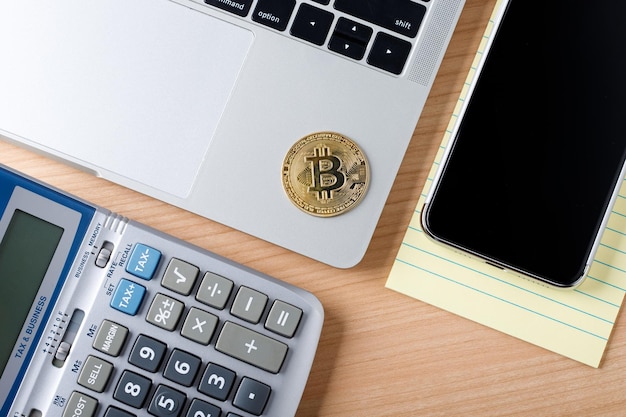 Bitcoin standard BTC crypto currency on laptop computer Top view mock up on wooden table with calculator and mobile cell phone paper note