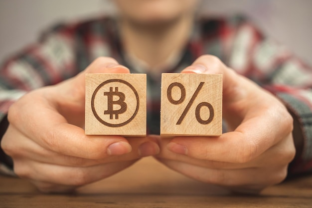 Bitcoin and taxes concept background Wooden cubes with bitcoin and percent symbols in hands closeup view business photo