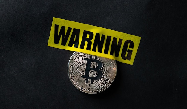 Bitcoin virtual currency coin and yellow caution tape with word warning concept of economy and money