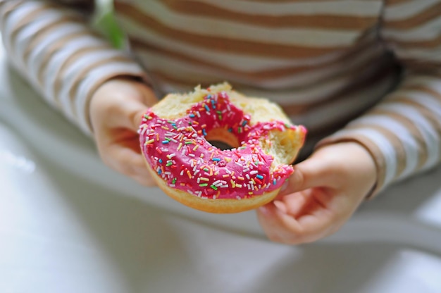 Bitten pink doughnut with strawberry taste in the hands of a small child, horizontal image with free space for text