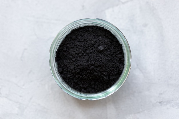 Black activated charcoal powder in a glass. Superfood, ingredient for cosmetics and vegan, vegetarian food, detox concept. Gray wall. Copy space, selective focus