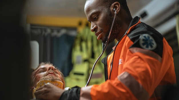 Black African American EMS Professional Paramedic Providing Medical Help to Injured Patient on the Way to Hospital Emergency Care Assistant Using Stethoscope in an Ambulance Hes Happy and Smiles