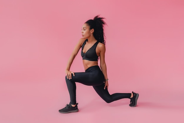 black african american woman in black leggings and top fitness outfit on pink