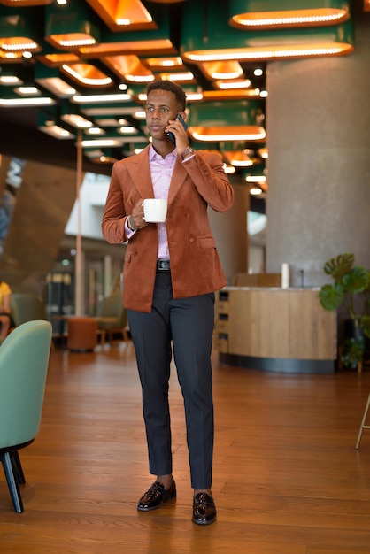 Black African businessman standing in coffee shop talking on phone full length shot