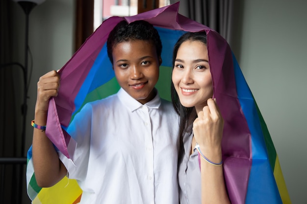 Black African LGBT woman holding LGBTQ rainbow flag with asian LGBT woman upside down new member of gay pride movement concept