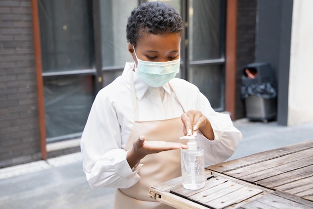 Black African woman shop keeper small business owner do a business reopening preparation work by wearing proper face mask and cleaning her hand with alcohol gel hand sanitizer before start working