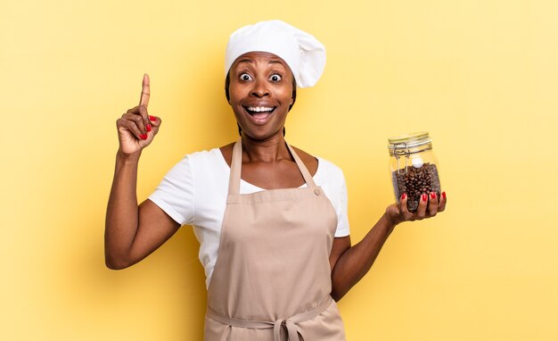 Black afro chef woman feeling like a happy and excited genius after realizing an idea, cheerfully raising finger, eureka!. coffee beans concept