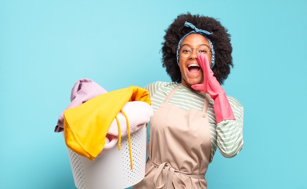 Black afro woman feeling happy, excited and positive, giving a big shout out with hands next to mouth, calling out. housekeeping concept.. household concept