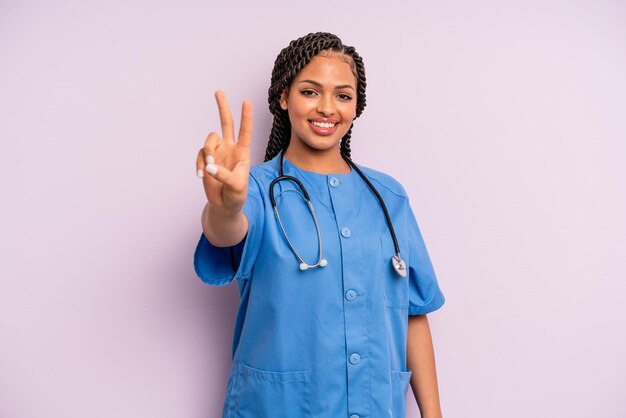 Black afro woman smiling and looking friendly showing number two nurse concept