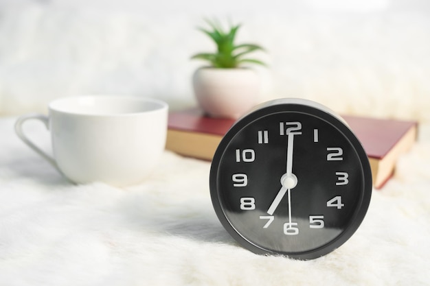 Black alarm clock and coffee cup with book on table