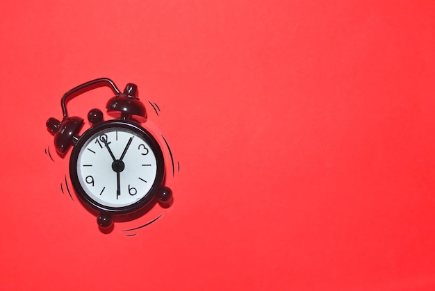 Black alarm clock on red background with loud and vibrating effect