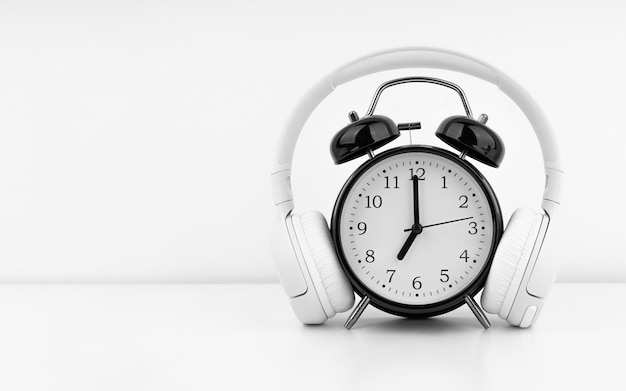 Black alarm clock with headphones on white wall background