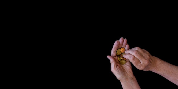 Black background with the hands of an elderly woman who holds coins copy paste