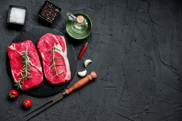 A black background with two raw steaks and a knife with garlic on it.