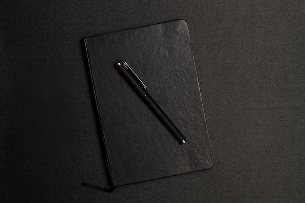 A black ballpoint pen on a black diary on a black background