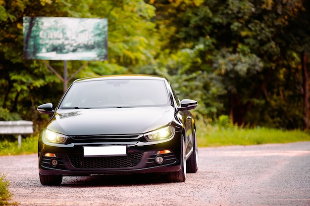 The black beautiful glossy car sedan rides on the road in the forest with no number and with headlights on. . High quality photo