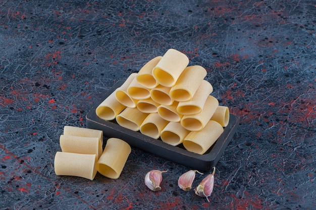 A black board of raw cannelloni pasta with garlic on a dark surface