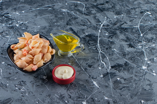 Black bowl of tasty seashell pasta with olive oil on marble surface. 