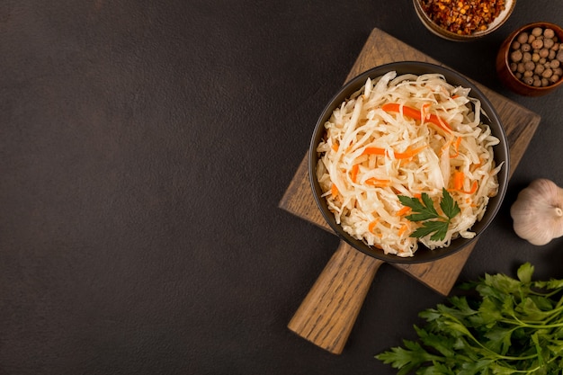 Black bowl with sour sauerkraut on wooden cutting board