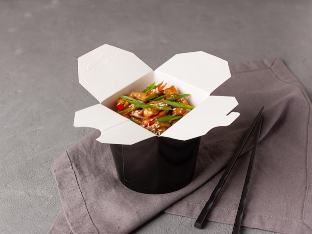 A black box of wok noodles with seafood on a gray background Food delivery