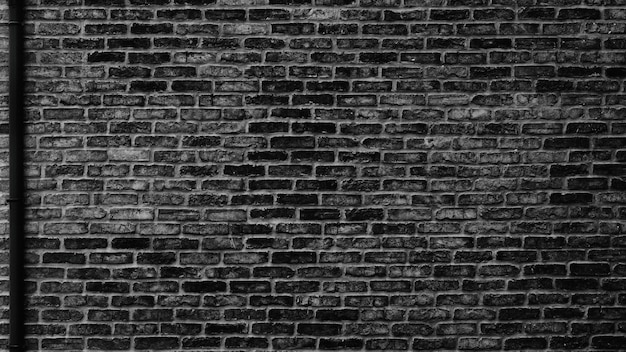 Black brick wall with drain pipe Dark brickwork texture Gloomy urban grunge background