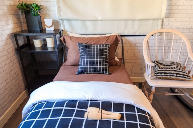 A black and brown pillow on a brown bed with a black steel shelf and wooden chair.