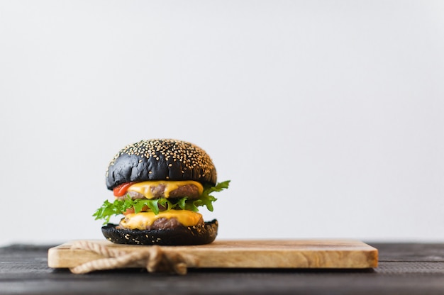 Black Burger on wooden chopping Board, grey background.